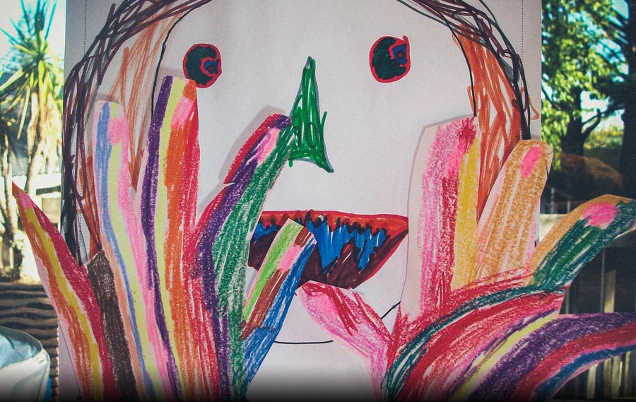 A picture drawn by a young child of a very colourful person putting their hands up and saying STOP